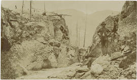 Man stands on a boulder in a small canyon with a rushing river