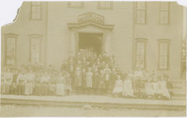 Group portrait of students and teachers outside the wood frame schoolhouse on Harris Street in Br...